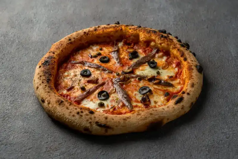 Homemade Napoli pizza topped with anchovies, olives, and fresh tomato sauce at Secret Oven restaurant
